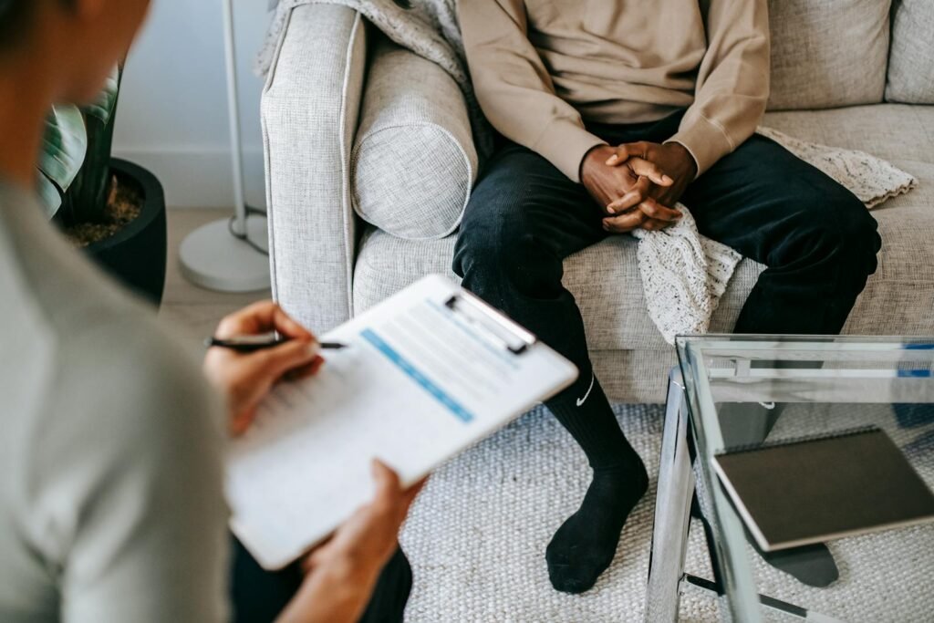 Therapist takes notes as client sits on a sofa during a psychotherapy session.