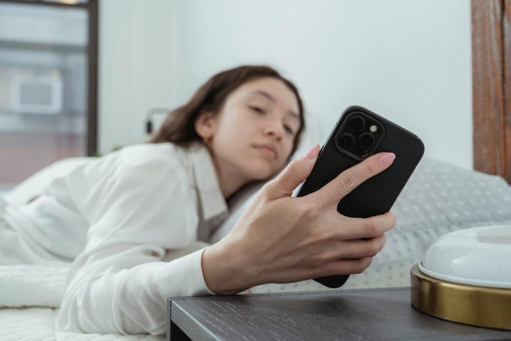 Caucasian woman relaxing in bed, holding mobile phone in morning light.