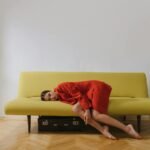 A woman in a red blazer rests on a minimalist yellow sofa indoors, evoking calmness.